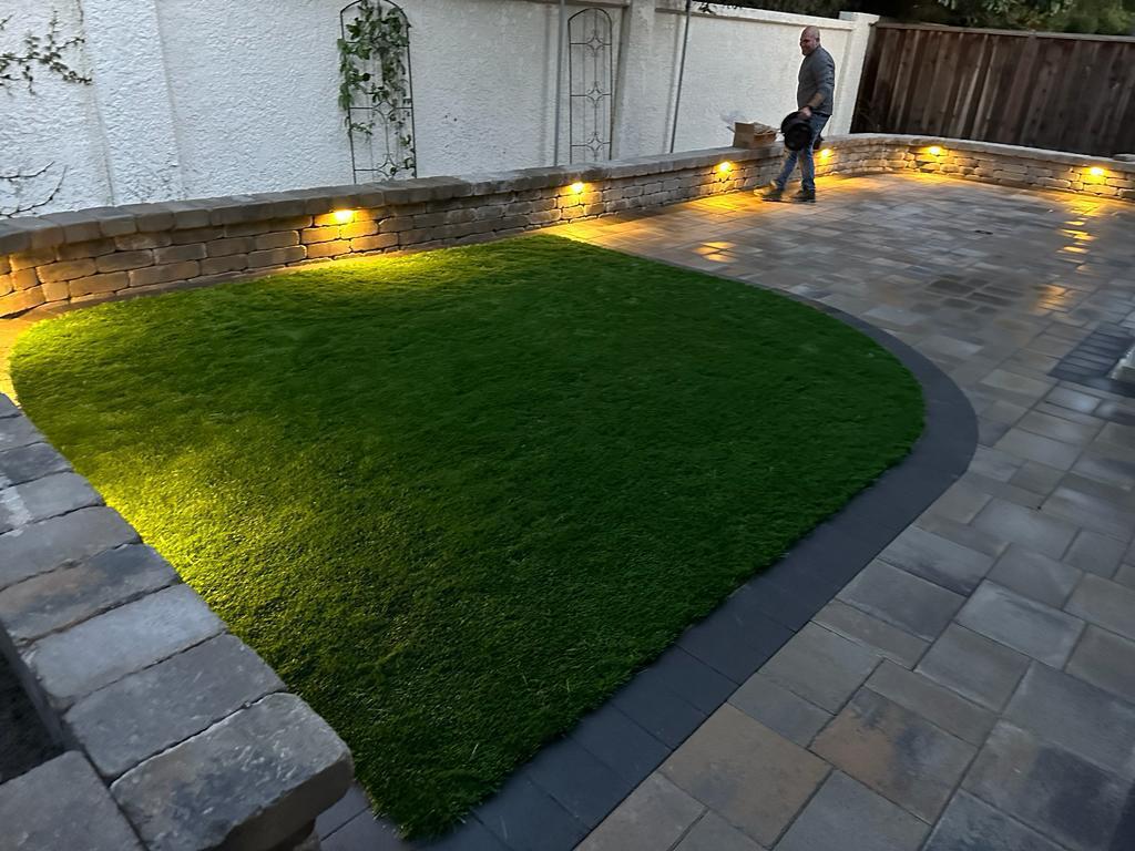 Paver patio with lit seating wall and lawn